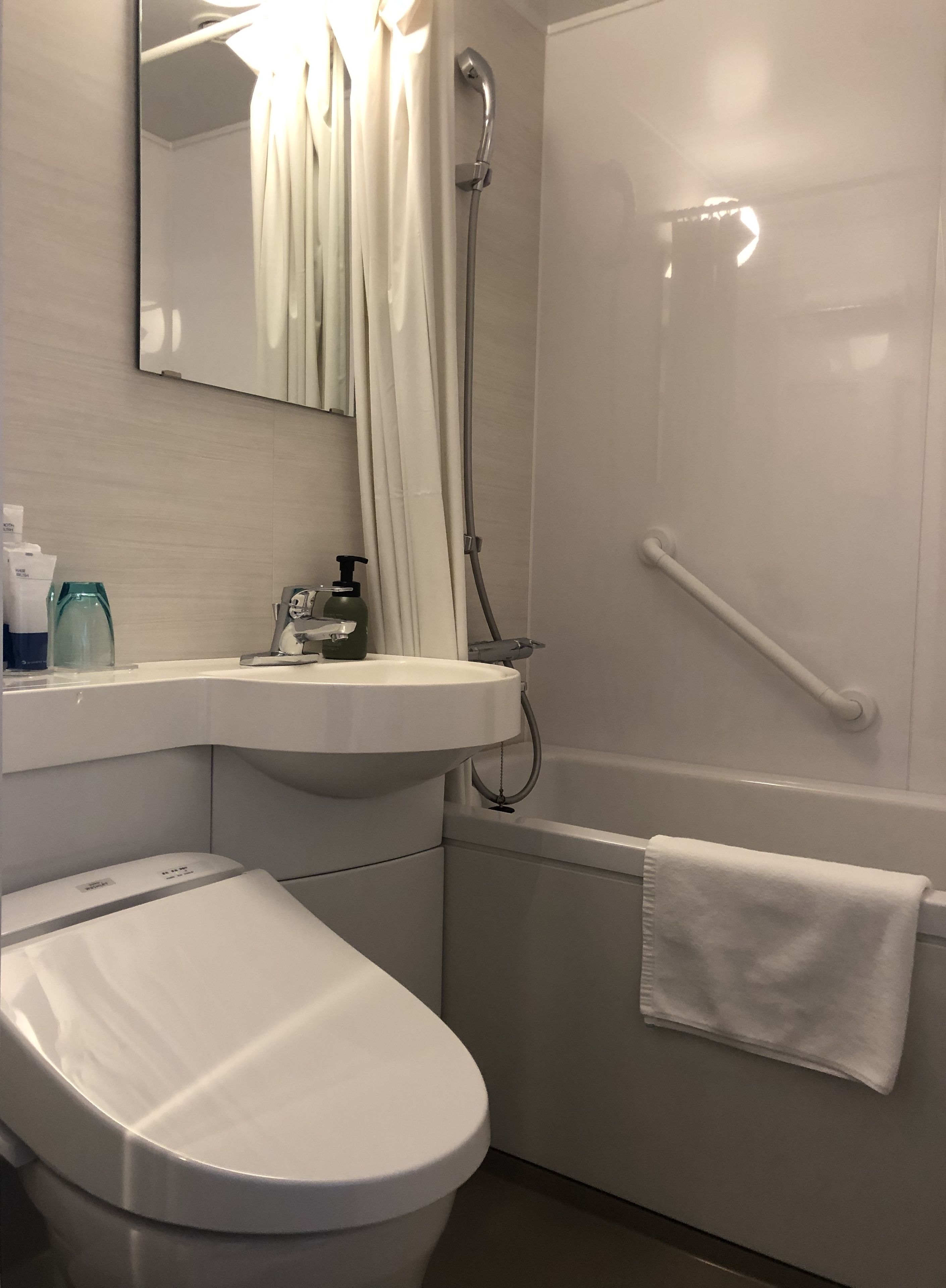 Un baño moderno con inodoro blanco, lavamanos, ducha y barandilla.