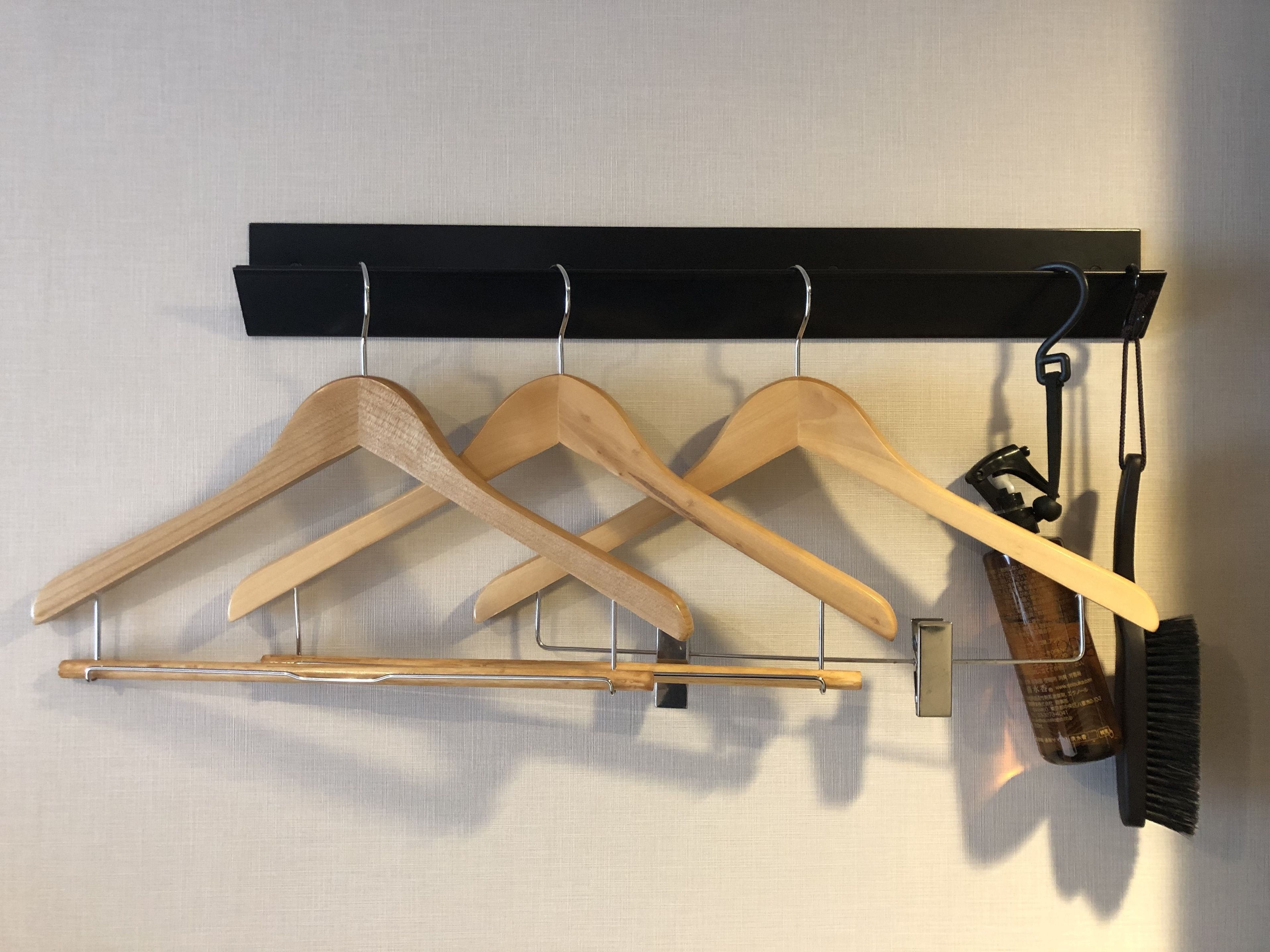 A wall-mounted wooden hanger rack with three hangers and a hairbrush.