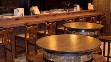 A bar area with wooden tables and chairs, a counter with books and papers, and a window in the background.