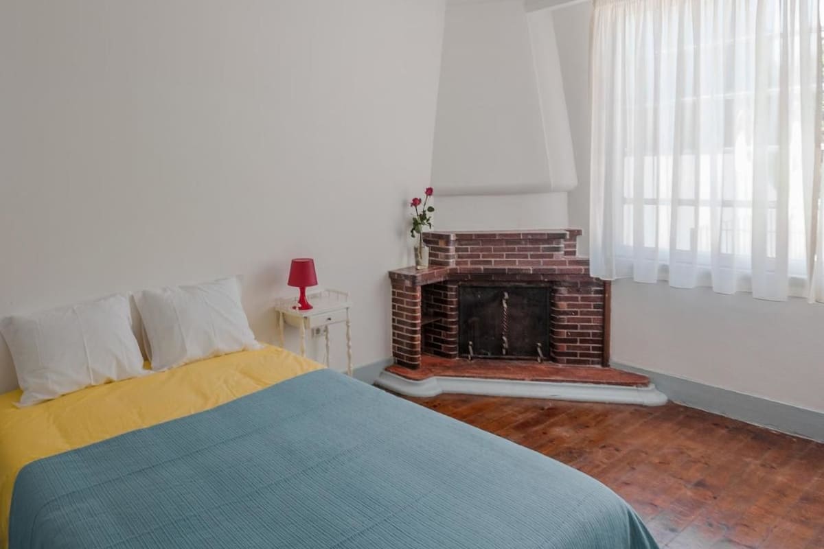 A bedroom with a bed, a fireplace, a window with sheer curtains, and a white ceiling with decorative molding.
