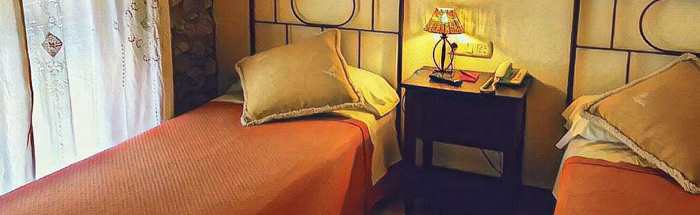 Habitación de hotel con dos camas individuales, una mesita de noche con lámpara y teléfono.