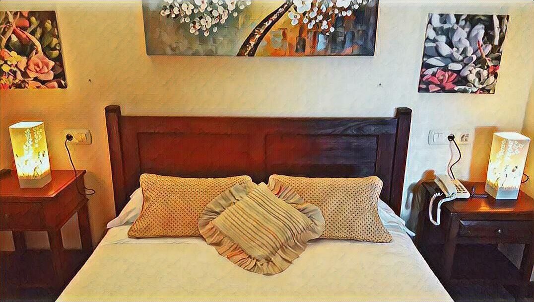Una cama impecable con dos almohadas y un edredón con flecos, un cabecero de madera y dos mesitas de noche con lámparas.