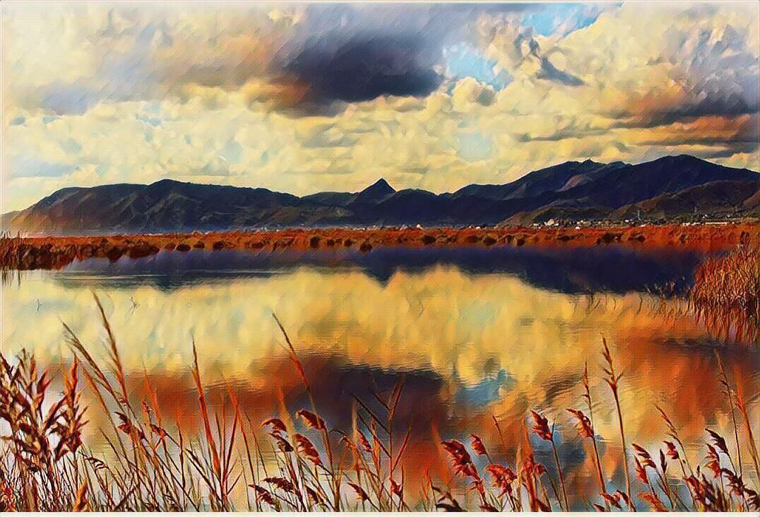 Un paisaje sereno con un lago tranquilo que refleja el cielo y montañas al fondo.
