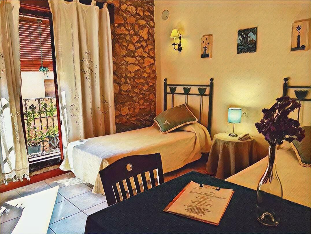 Una habitación con dos camas individuales, una mesita con lámpara, una silla y un florero con flores.