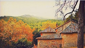 Un bâtiment en pierre, surmonté d’un toit en tuiles, entouré d’arbres aux feuilles d’automne.