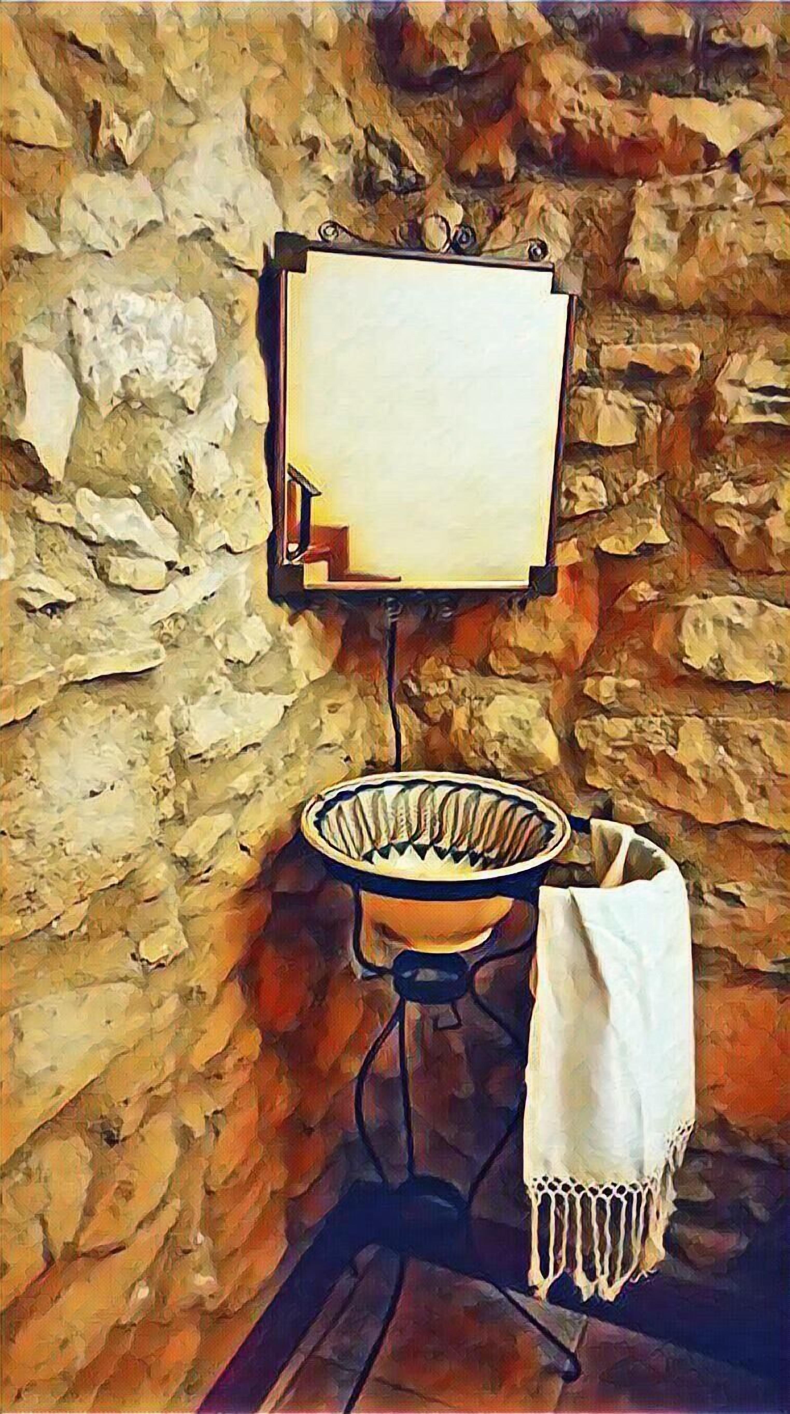 A stone wall with a framed picture hanging on it. Below the picture, there is a white basin with a blue stand. A white cloth is draped over the stand.