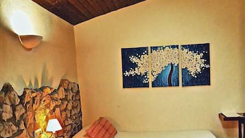 Een gezellige kamer met een stenen muur, een bed, een tafel met een lamp en een schilderij aan de muur.