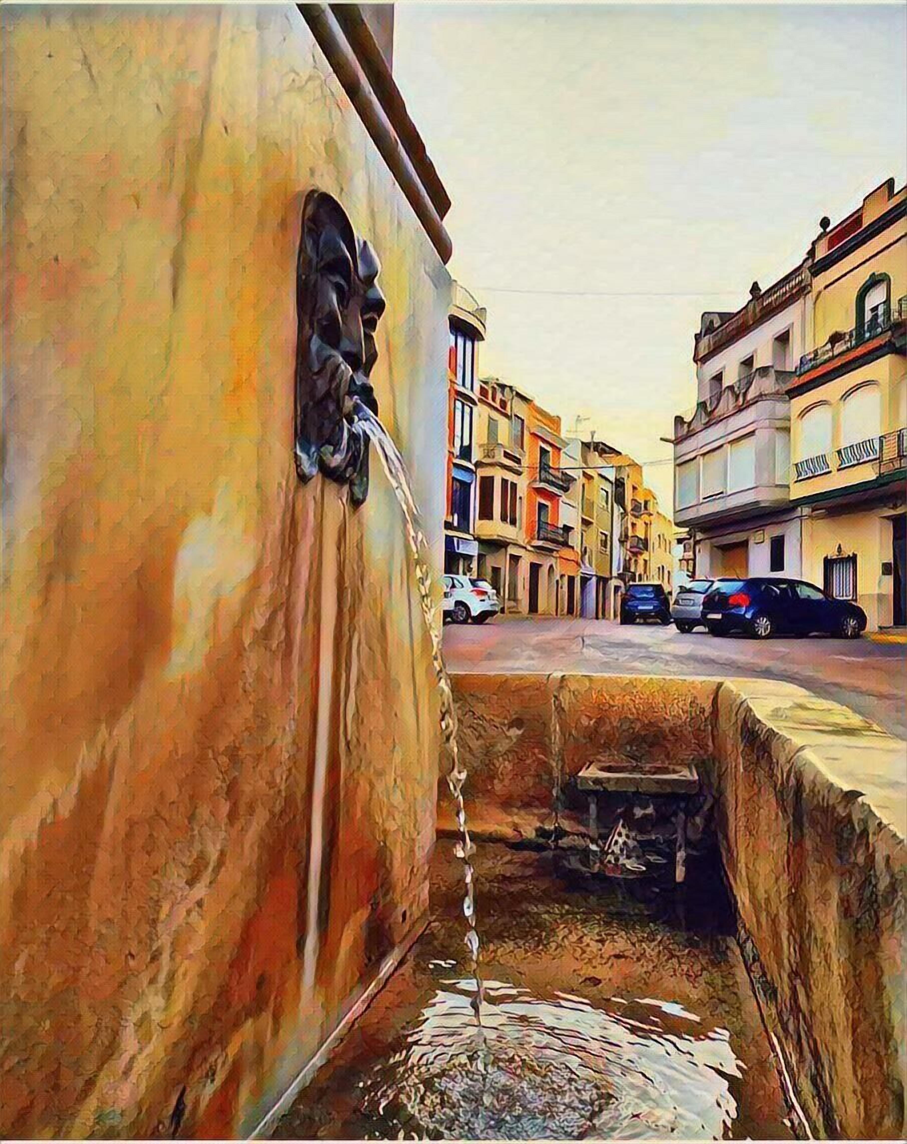 Vista de una calle con edificios, un chorro de agua y automóviles estacionados.