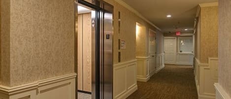 Un pasillo de hotel con piso alfombrado, paneles blancos y una puerta que da a una habitación.