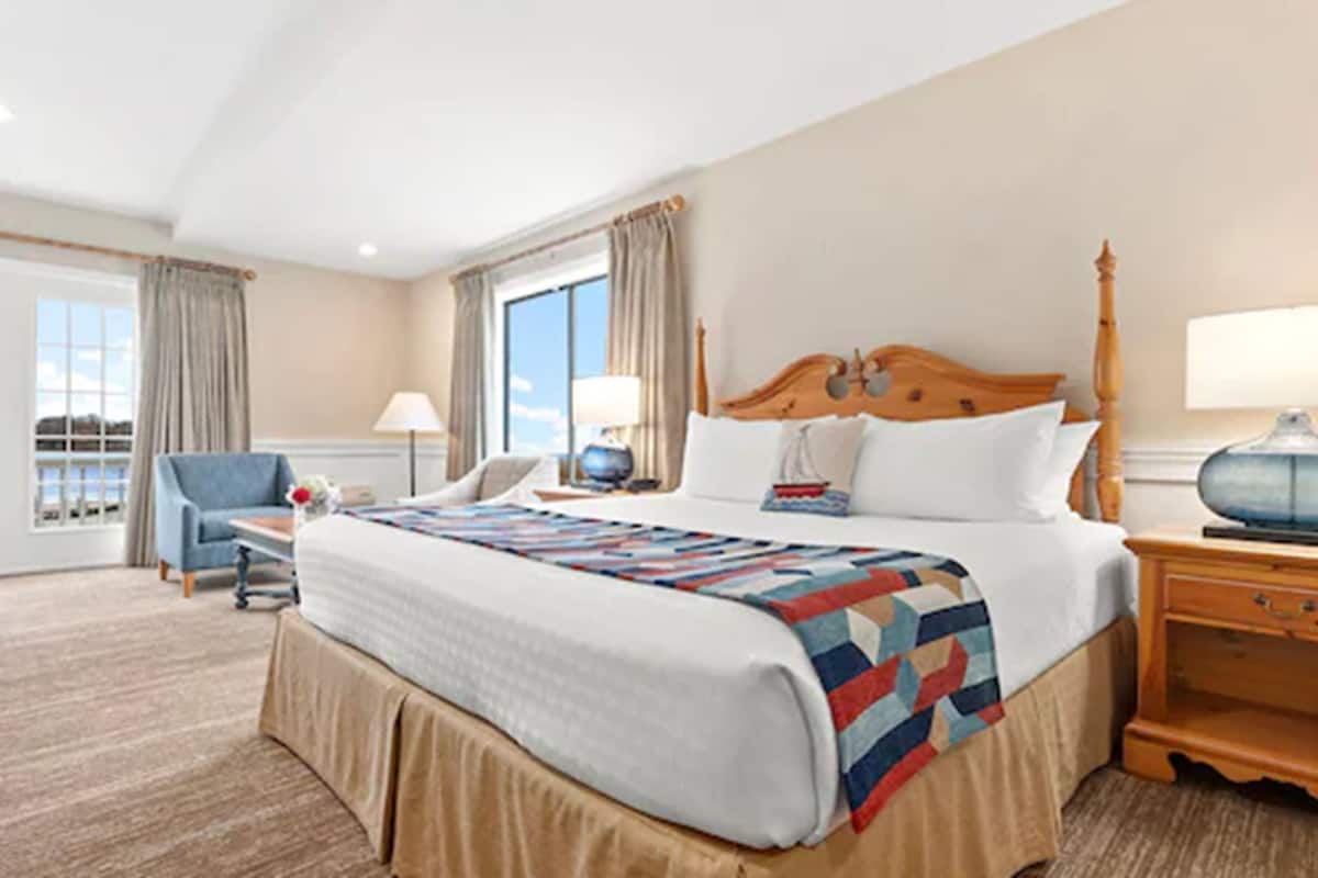 A hotel room with a large bed, a desk, a chair, and a view of the outdoors through the windows.