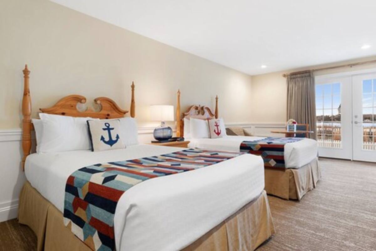 A hotel room with a large bed, two bedside tables, a nightstand, a lamp, and a view of the outdoors through a sliding glass door.