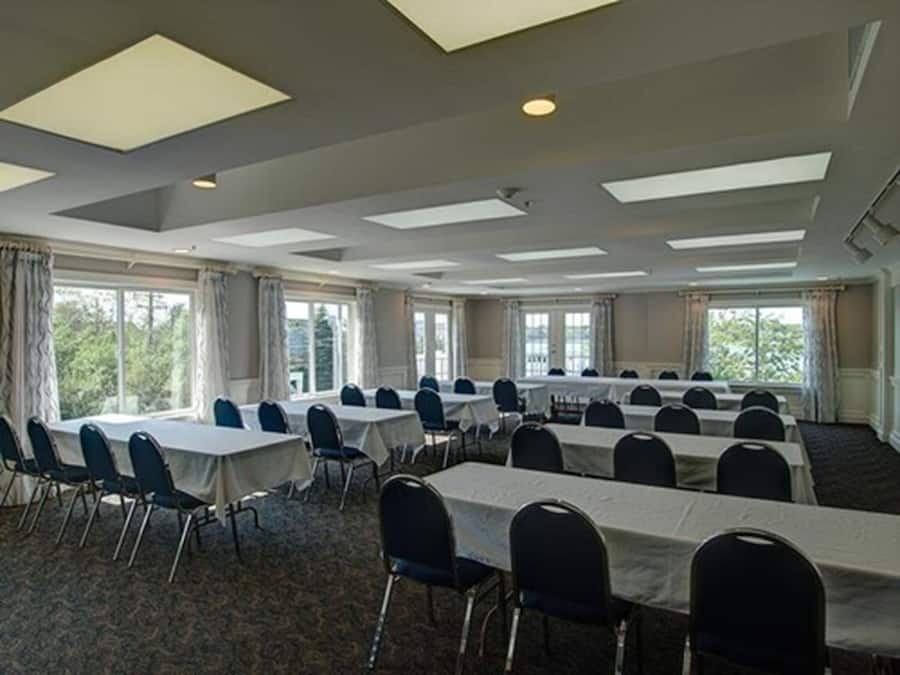 A conference room with multiple tables and chairs, large windows, and a high ceiling with skylights.