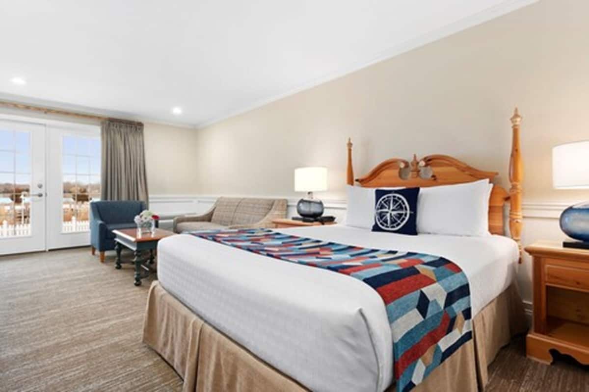 A hotel room with a large bed, a desk, a chair, a lamp, and a view of the outdoors.