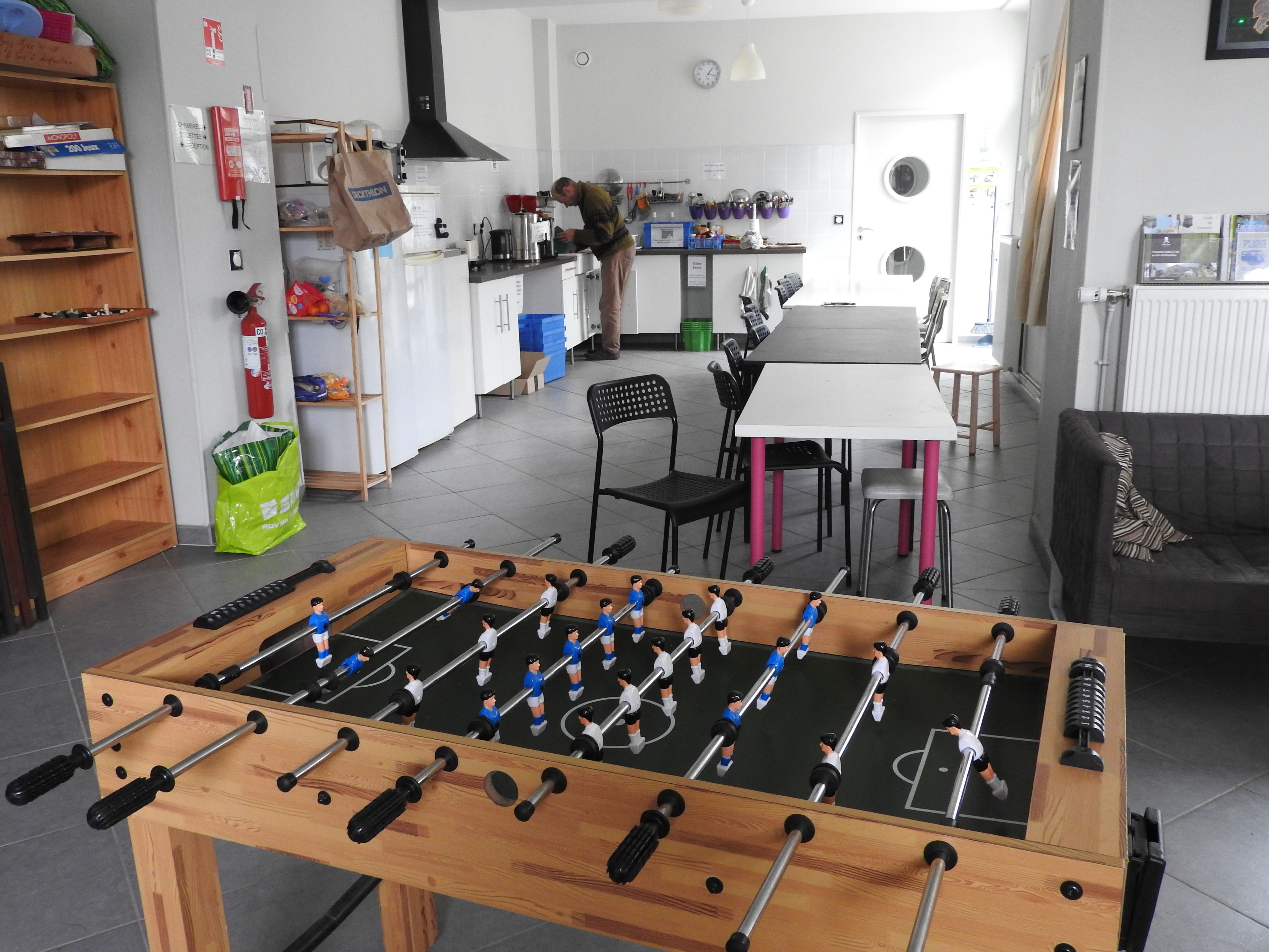 A room with a foosball table, a kitchen area, and a dining table with chairs.