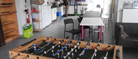 A room with a foosball table, a kitchen area, and a dining table with chairs.