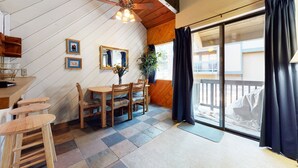 Een gezellige kamer met een houten eettafel, stoelen en een kleine keukenhoek met een spoelbak en aanrecht.