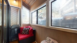 A cozy corner with a red cushioned bench, a wicker chair, and a view of a snowy street through large windows.