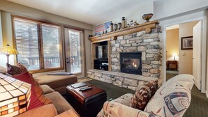 A cozy living room with a stone fireplace, comfortable seating, and a television. - Mammoth Green #111 2 Bedroom Condo (Mammoth Lakes)
