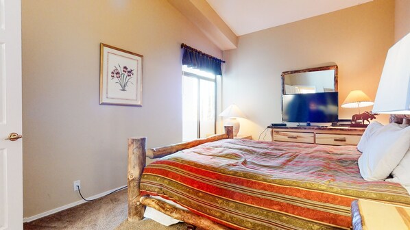 Quarto com estrutura de cama de madeira, televisão, abajur e quadro na parede.