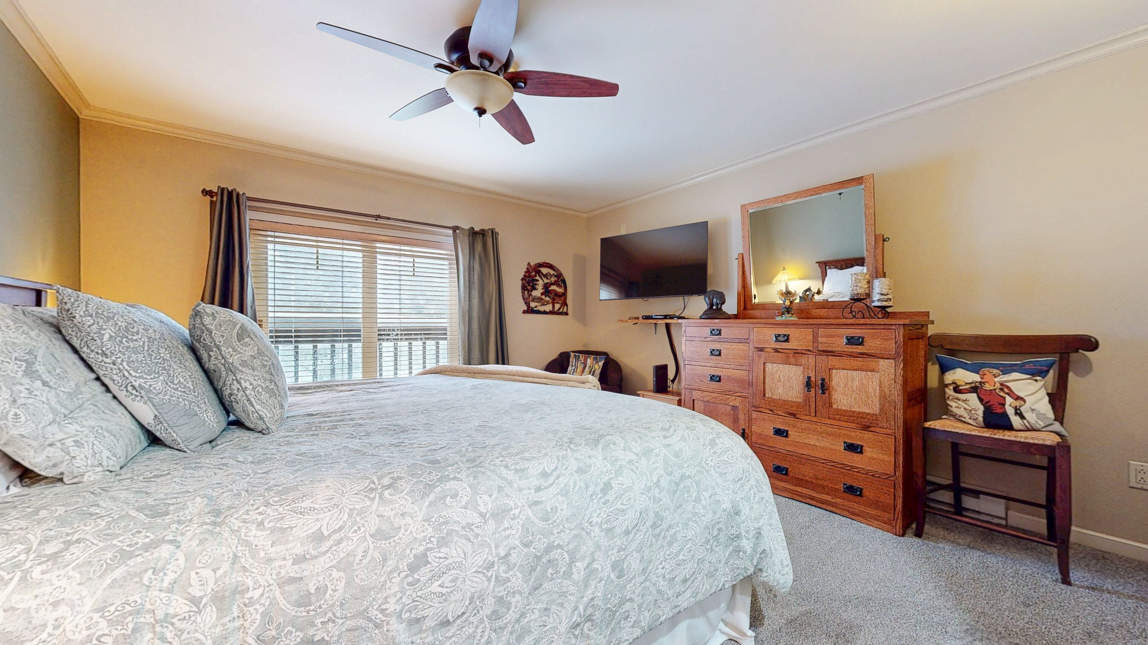 A bedroom with a bed, a dresser, a chair, a television, and a ceiling fan.