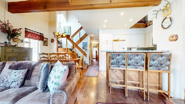 A spacious living area with a wooden staircase, a kitchen with white cabinets, and a dining area with patterned chairs. - Snowcreek #638 3 Bedroom Condo (Mammoth Lakes)