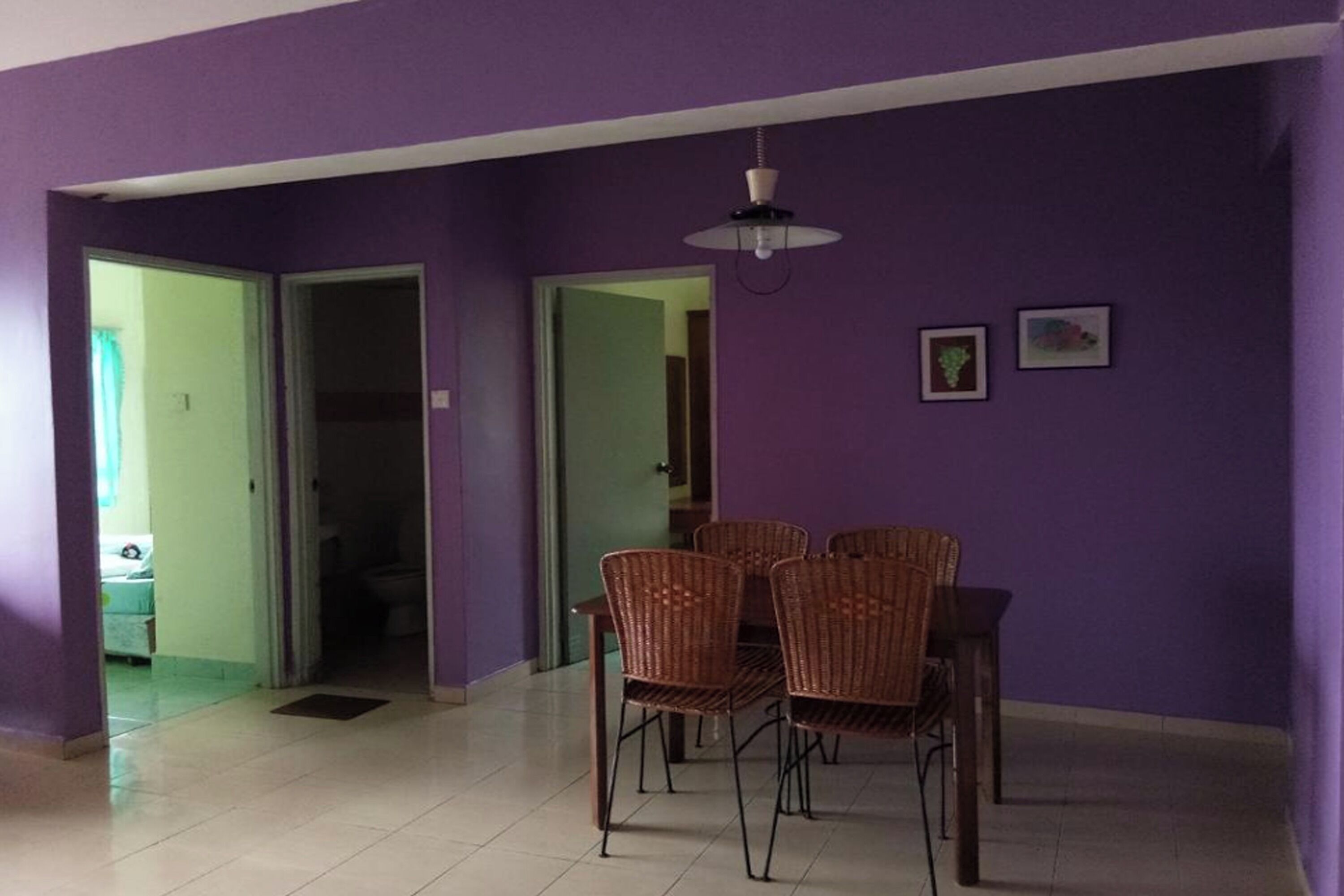 A dining area with wicker chairs and a table, purple walls, and a ceiling light.