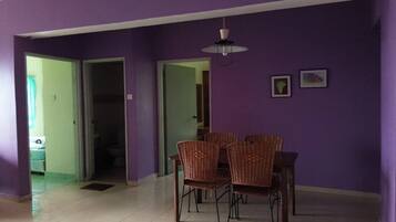 A dining area with wicker chairs and a table, purple walls, and a ceiling light.