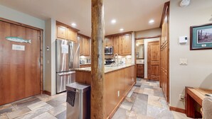 A modern kitchen with wooden cabinets, stainless steel appliances, and a stone tile floor.