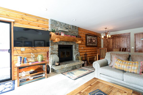 Ein gemütliches Blockhaus-Interieur mit Kamin aus Stein, einer Couch und einem Bücherregal.