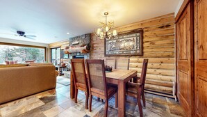 A cozy dining area with a wooden table and chairs, a chandelier, and a stone fireplace.