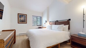 A bedroom with a bed, a desk, a chair, a window with blinds, and a painting on the wall.