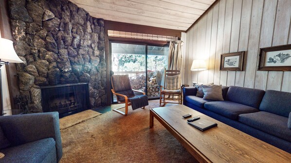 A cozy living room with a stone wall, a fireplace, a blue sofa, and a wooden coffee table.