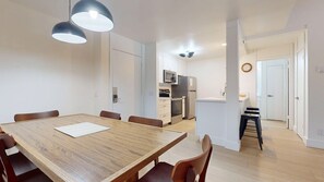 A modern kitchen with white cabinets, a microwave, stove, and refrigerator. There is a dining area with a wooden table and chairs.
