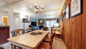 A dining area with a wooden table and chairs, a chandelier, and a television in the background. - Summit #45 1 Bedroom Condo (Mammoth Lakes)