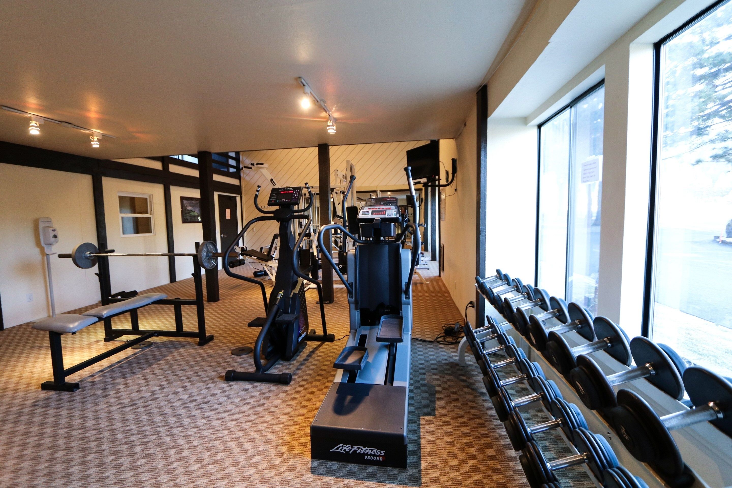 A gym with cardio machines, weightlifting equipment, and a bench.