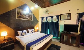 A hotel room with a bed, a TV, a desk, a lamp, a painting, and a window with curtains. - Kangs Nirvana Resorts and Spa (Garhshankar)