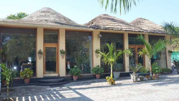A building with a thatched roof, large windows, and potted plants in the foreground. - Kangs Nirvana Resorts and Spa (Garhshankar)