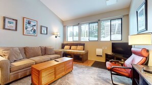 A cozy living room with a sofa, a wooden coffee table, a bench, and a TV.