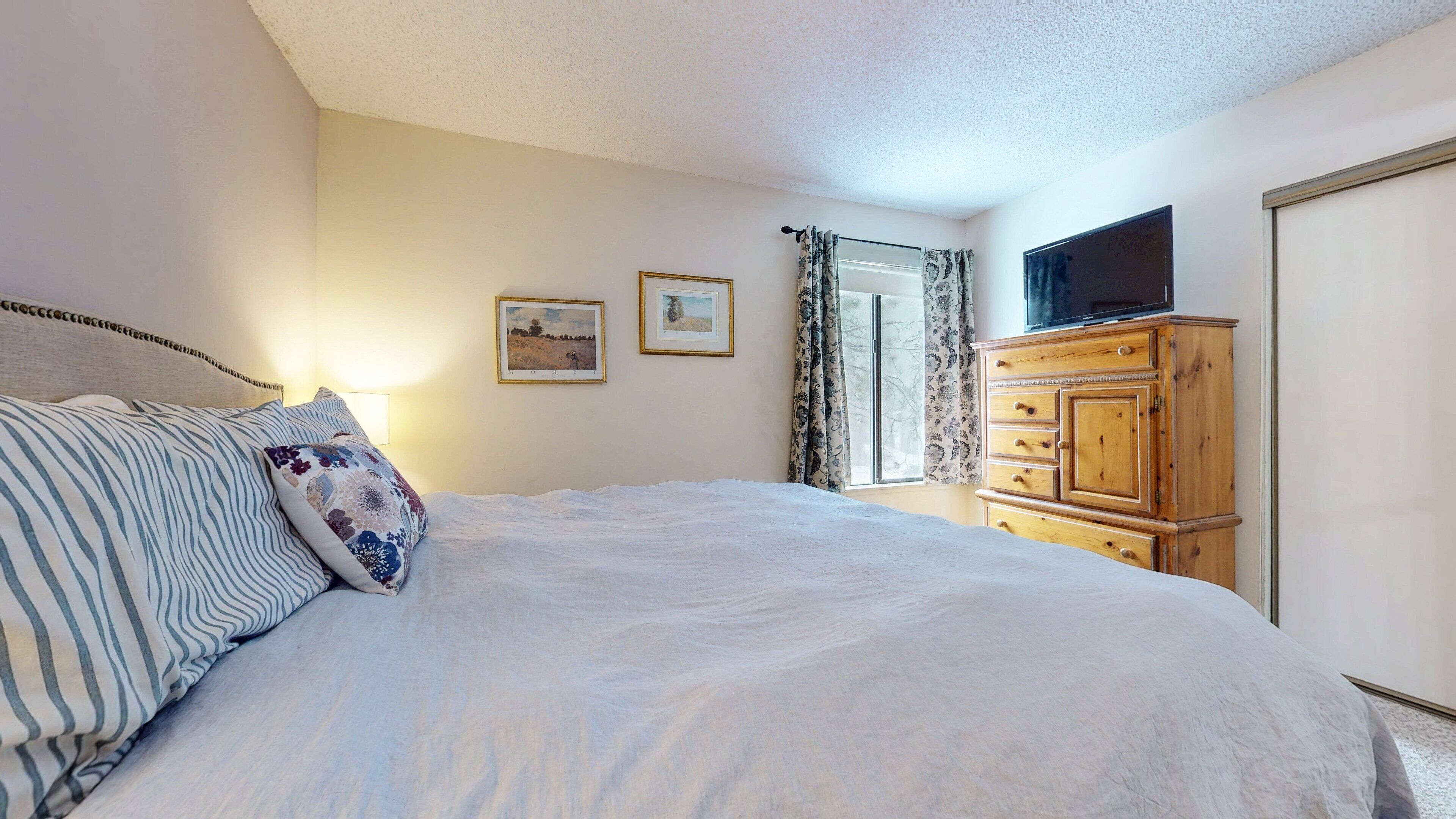 A bedroom with a bed, a wooden dresser, a television, and two framed pictures on the wall.
