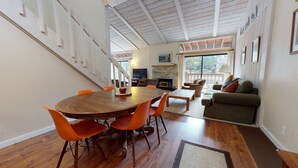 Uma sala de estar ampla, com uma mesa de jantar de madeira, cadeiras laranja, um sofá e uma lareira.