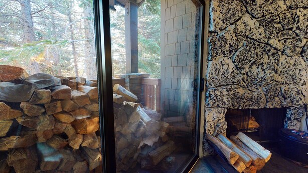 A room with a fireplace, a glass door leading outside, and a pile of firewood. - Summit #280 2 Bedroom Condo (Mammoth Lakes)