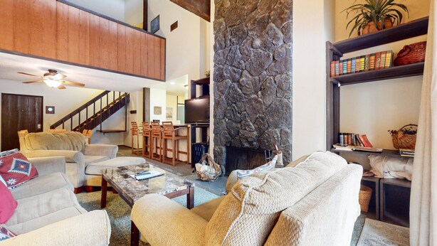 A spacious living room with a stone fireplace, a high ceiling with wooden beams, and a cozy seating area with a coffee table and chairs.