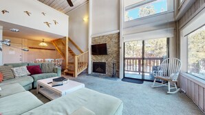 A spacious living room with a stone fireplace, a staircase, and a balcony with a view of trees. - Summit #98 3 Bedroom Condo (Mammoth Lakes)