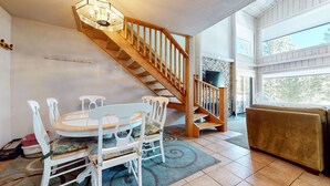 A dining area with a wooden staircase, a round table with chairs, and a sofa. - Summit #98 3 Bedroom Condo (Mammoth Lakes)