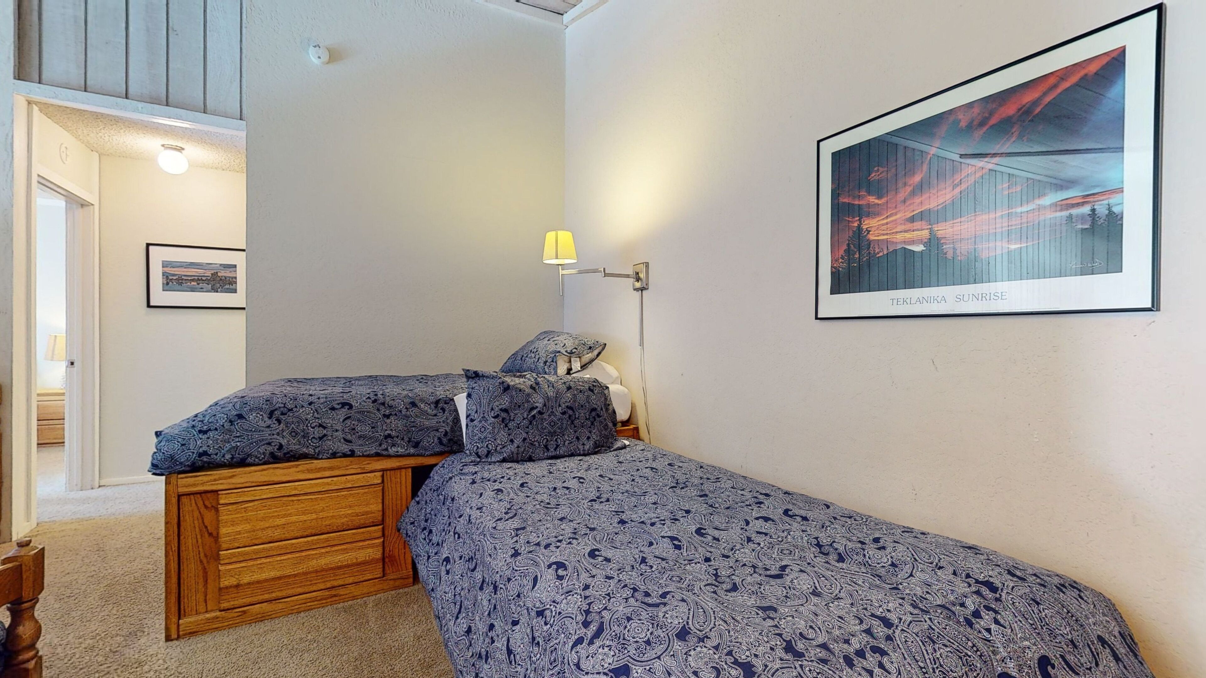 A bedroom with two beds, a nightstand, a lamp, and a framed picture on the wall.