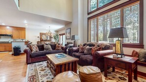 Ein geräumiges Wohnzimmer mit einer dunkelbraunen Ledersofa, einem Holztisch und einem gemusterten Teppich. Es gibt eine Essecke mit einem Holztisch und Stühlen, und eine Küche im Hintergrund.