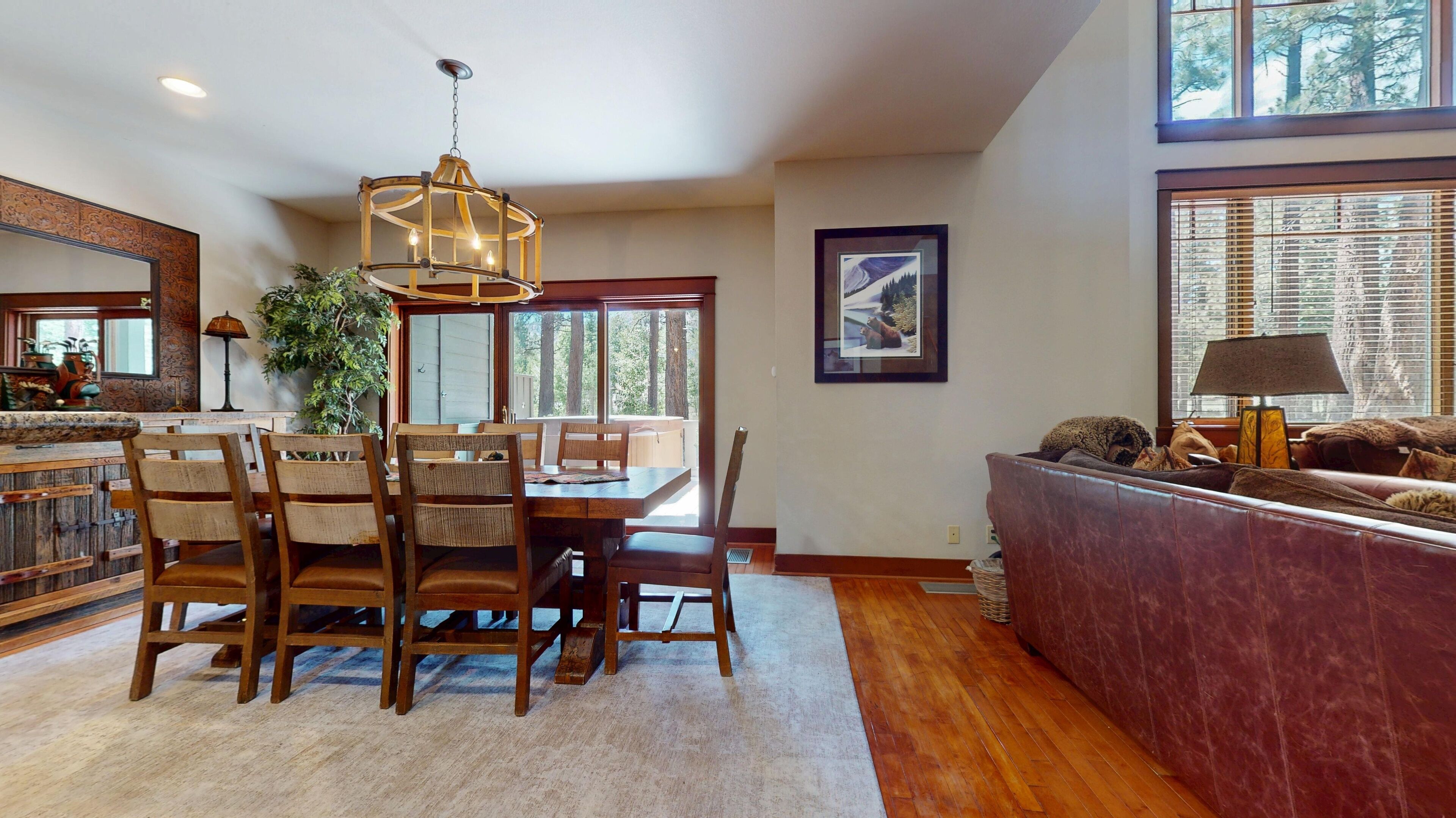 A dining area with a wooden table and chairs, a chandelier, and a large window with blinds.