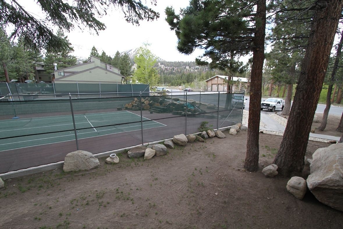 A tennis court with a net, surrounded by a fence and trees.