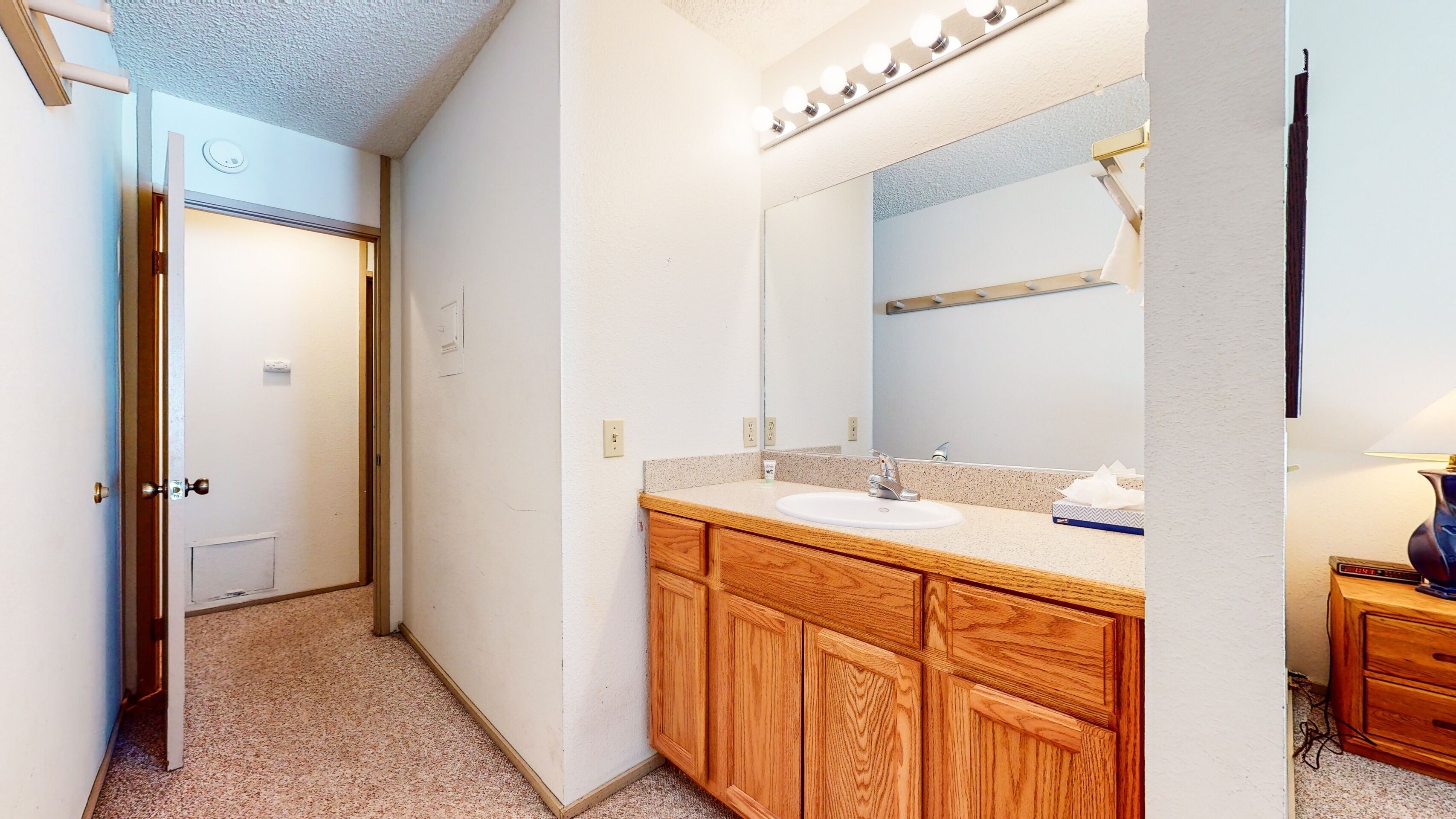 A bathroom with a wooden vanity, a sink, and a mirror with lights above it.