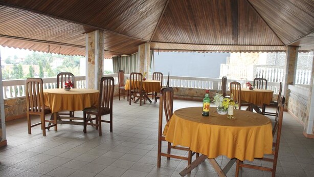 Un espacio comedor al aire libre cubierto con varias mesas redondas y sillas, suelo de baldosas y vistas del paisaje circundante.